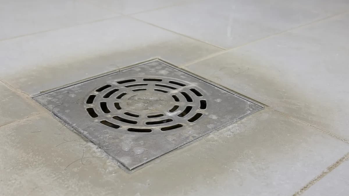 Ebenerdige Dusche mit Abflussrost aus Edelstahl – Detailaufnahme des Ablaufs mit leicht stehendem Wasser als Hinweis auf eine Verstopfung