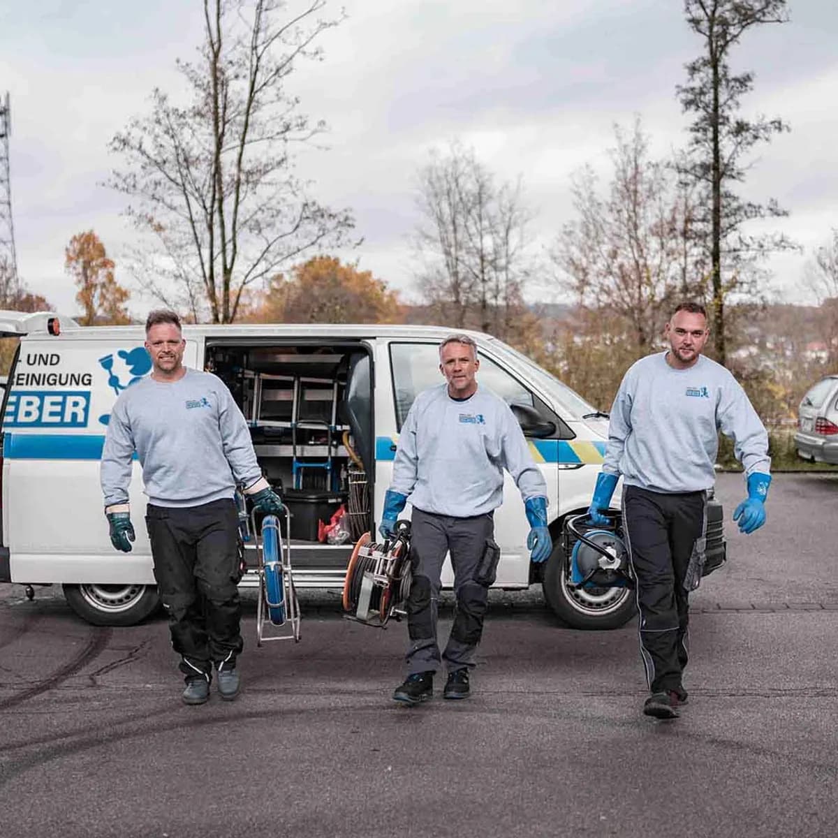 Drei Techniker von Kanal- und Rohrreinigung Bieber GmbH tragen Reinigungstechnik vom Einsatzfahrzeug